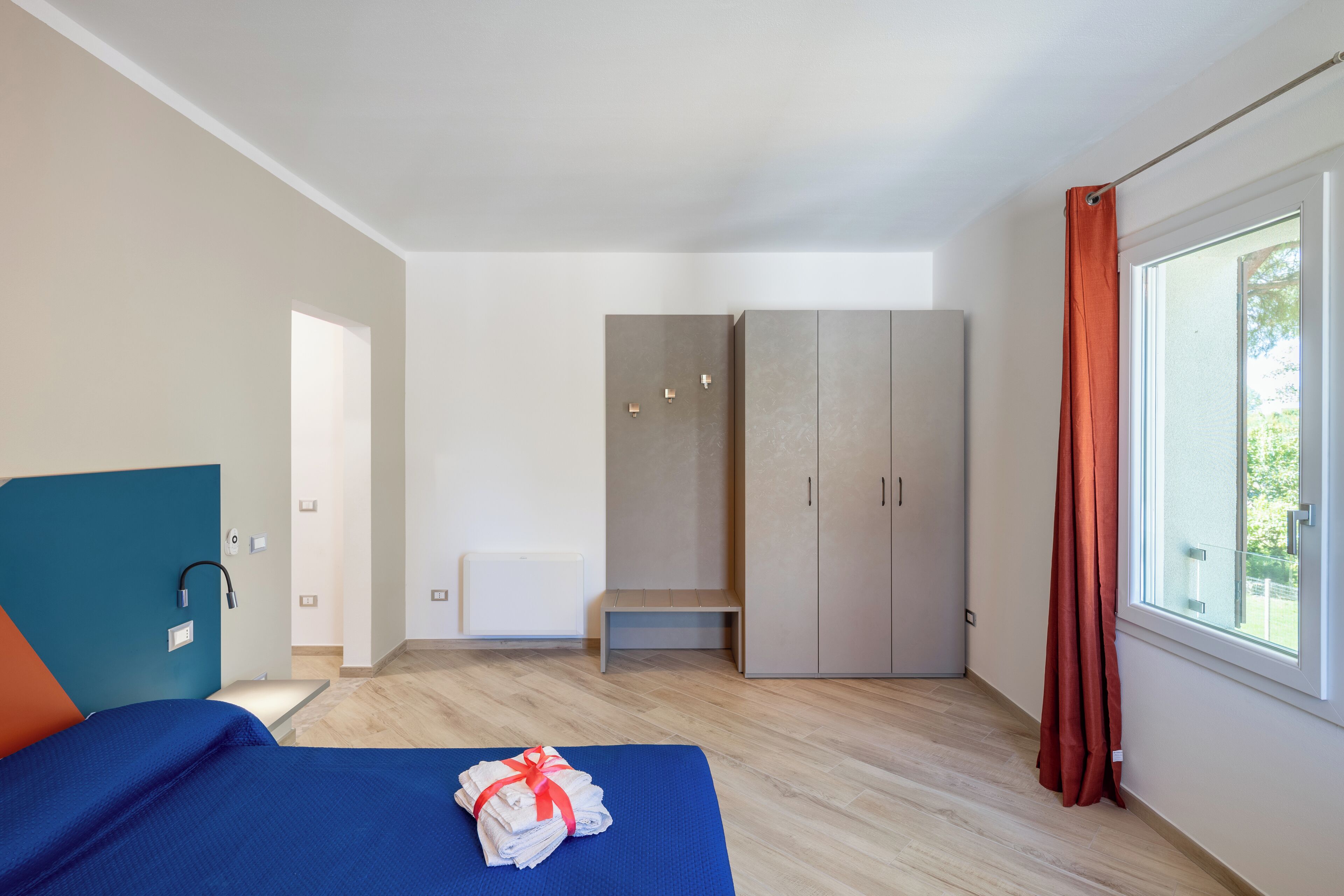 Una camera d'albergo moderna con un letto, una panca, un armadio e una finestra con tende.