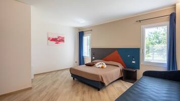 A modern hotel room with a bed, a bedside table, a window with curtains, and a wall-mounted artwork.