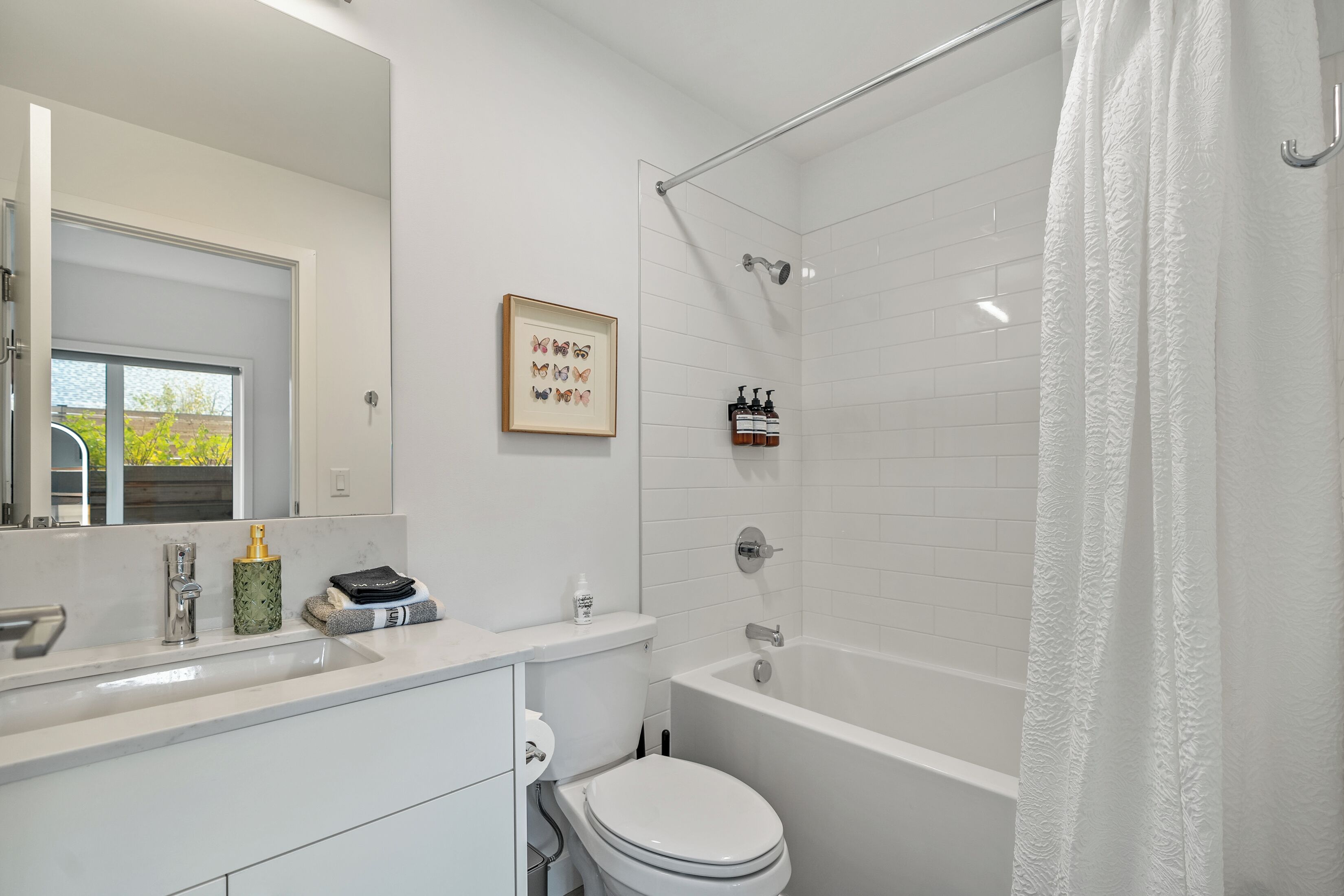 A modern bathroom with a white sink, toilet, and bathtub. There is a framed picture on the wall and toiletries on the counter.