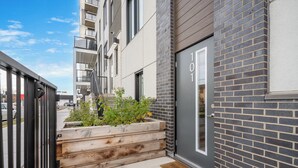 A modern building with a grey brick facade, a wooden planter with greenery, and a door marked "101". - ✨ The Era City Haven – Modern 2BR/2BA w/ Breathtaking Calgary Views (Calgary)