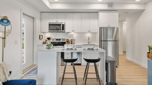 A modern kitchen with white cabinetry, stainless steel appliances, and a central island with bar stools. - ✨ The Era City Haven – Modern 2BR/2BA w/ Breathtaking Calgary Views (Calgary)