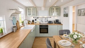 Une cuisine moderne avec des meubles de couleur vert clair, un plan de travail en bois et un coin repas avec une table dressée pour deux personnes.