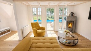 Un salon spacieux avec un canapé jaune, une cheminée et de grandes fenêtres donnant sur une piscine.