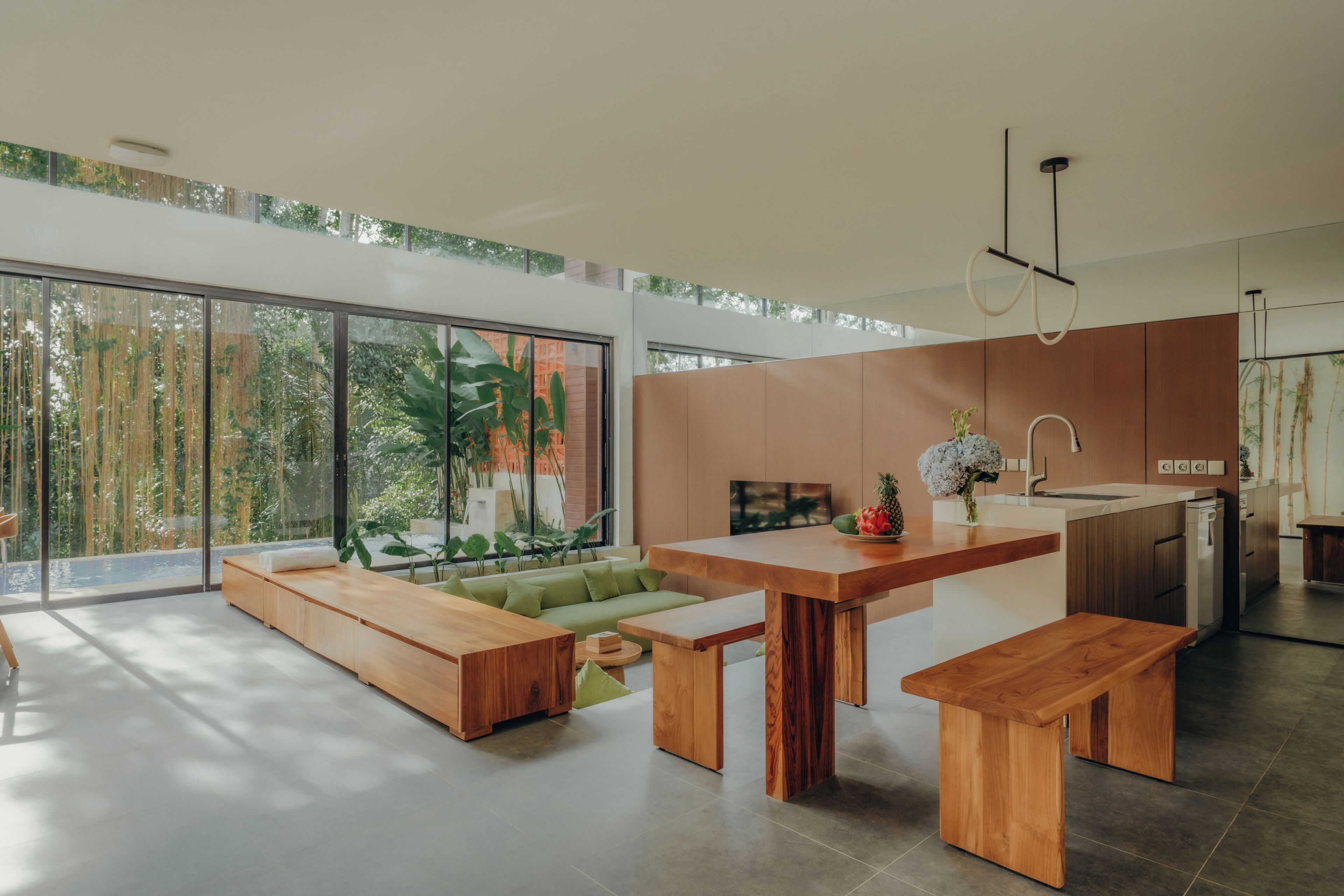 A modern kitchen with a large island, wooden furniture, and a view of greenery outside.