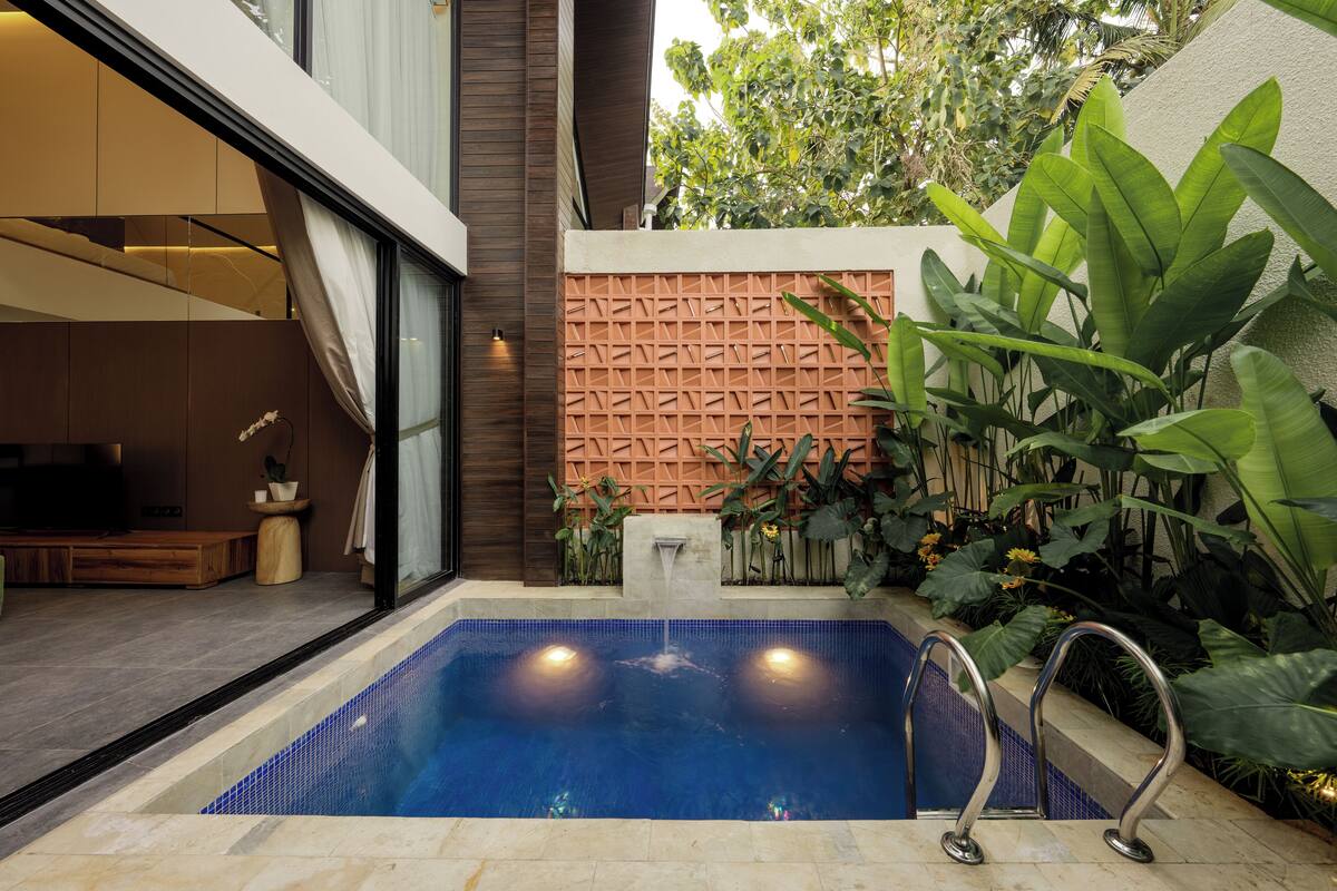 A modern pool area with a blue-tiled pool, a wooden deck, and a wall with a geometric pattern.