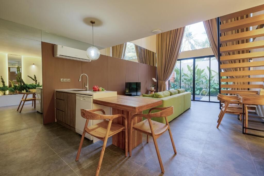 A modern kitchen with wooden cabinets, a dining area with a wooden table and chairs, and a large window with curtains.