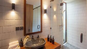 Un baño con un espejo grande, un lavabo de piedra y una zona de ducha.
