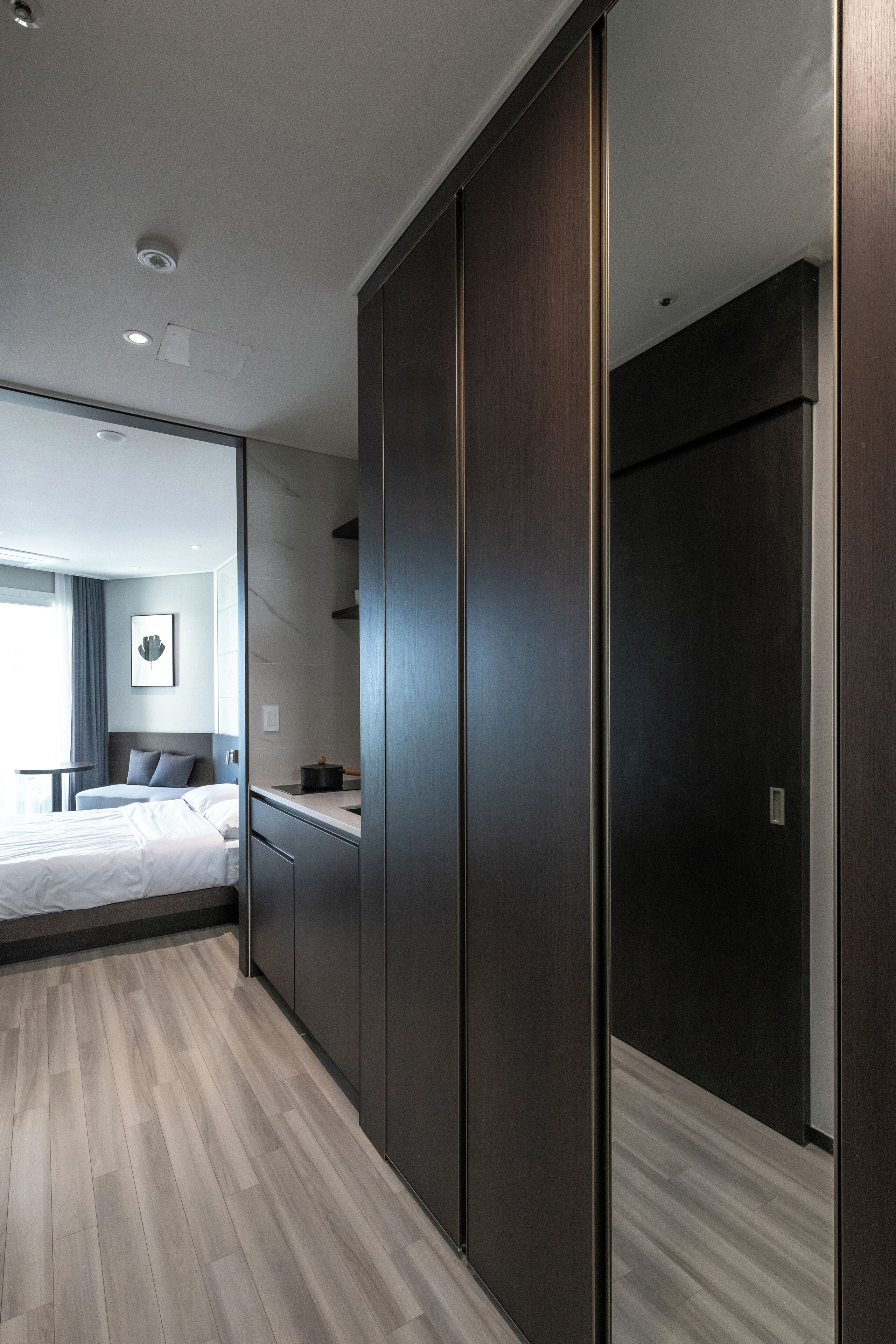 Moderni hotellihuone, jossa on sänky, työpöytä, vaatekaappi ja näkymä viereiseen huoneeseen.