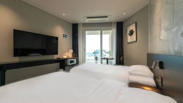 A hotel room with two beds, a flat-screen TV, a desk with a lamp, and a view of the city.