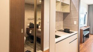 Ein modernes Hotelzimmer mit Holzboden, einer Küchenzeile, einem großen Spiegel und einer Schiebetür zu einem Badezimmer.