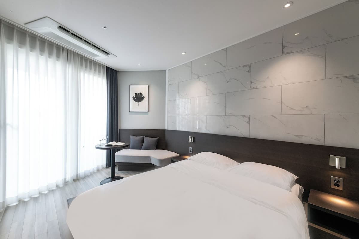 A modern hotel room with a large bed, a bedside table, a small desk, and a wall-mounted air conditioning unit.