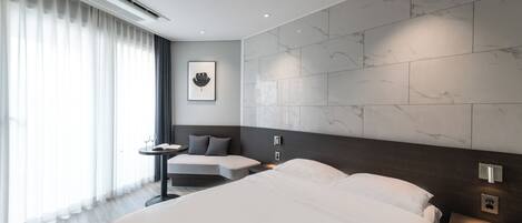 A modern hotel room with a large bed, a bedside table, a small desk, and a wall-mounted air conditioning unit.