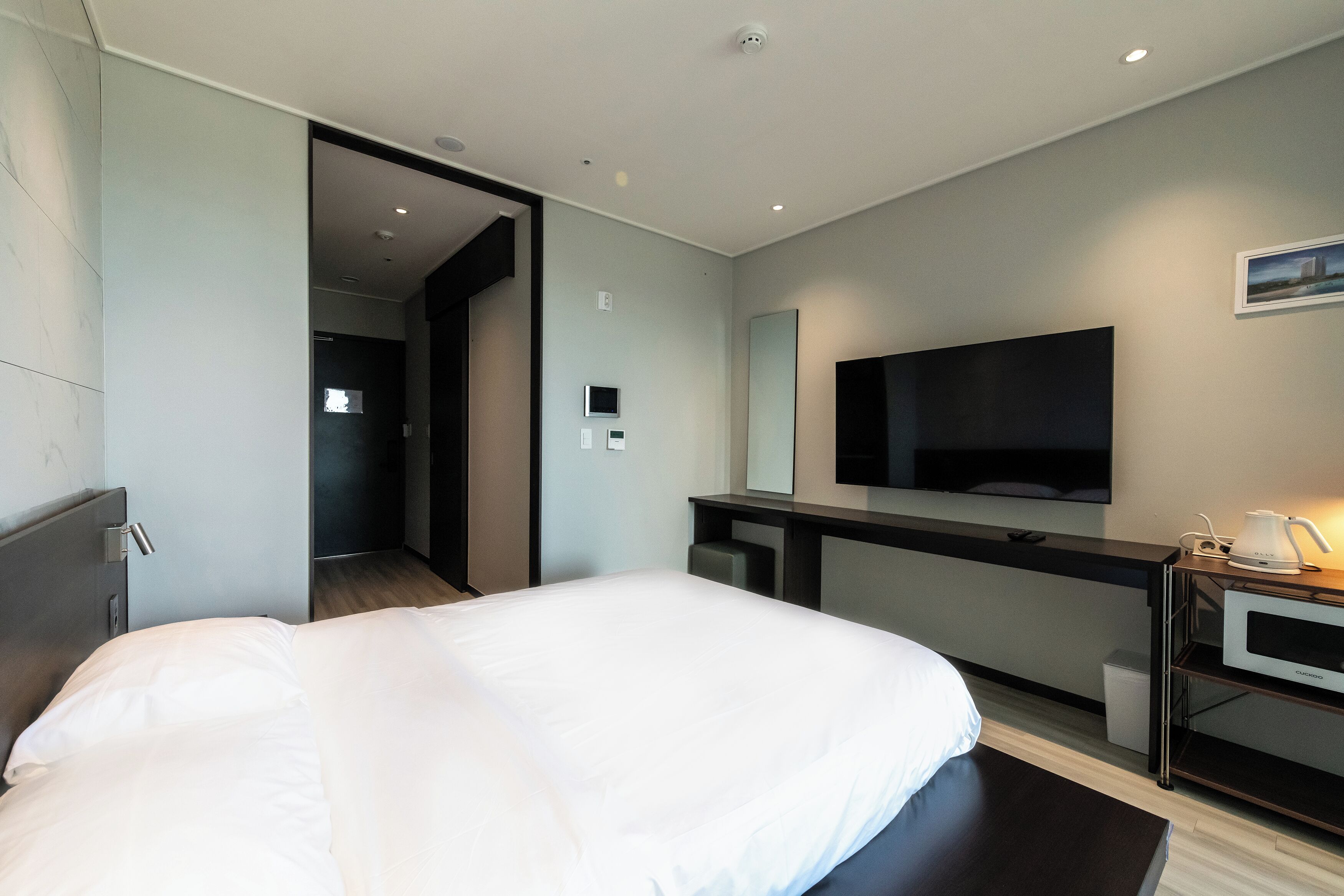 A modern hotel room with a large bed, a flat-screen TV, a desk with a coffee maker, and a walk-in closet.