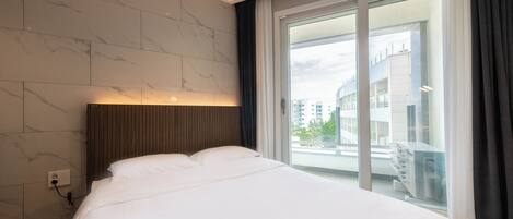 Een moderne hotelkamer met een groot bed, een houten hoofdeinde en stadszicht door een groot raam.