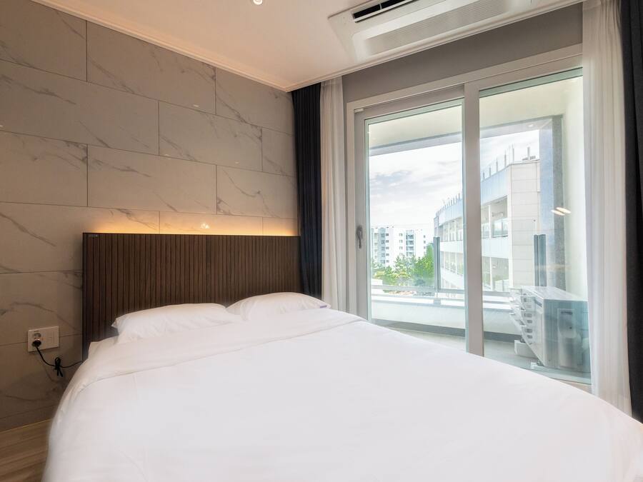 Una habitación de hotel moderna con una cama grande, cabecera de madera y vistas a la ciudad a través de un amplio ventanal.