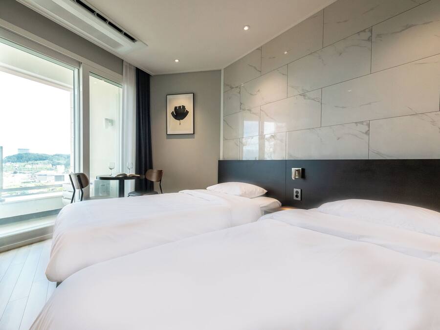 A hotel room with two beds, a large window with a city view, a small table, and a chair.