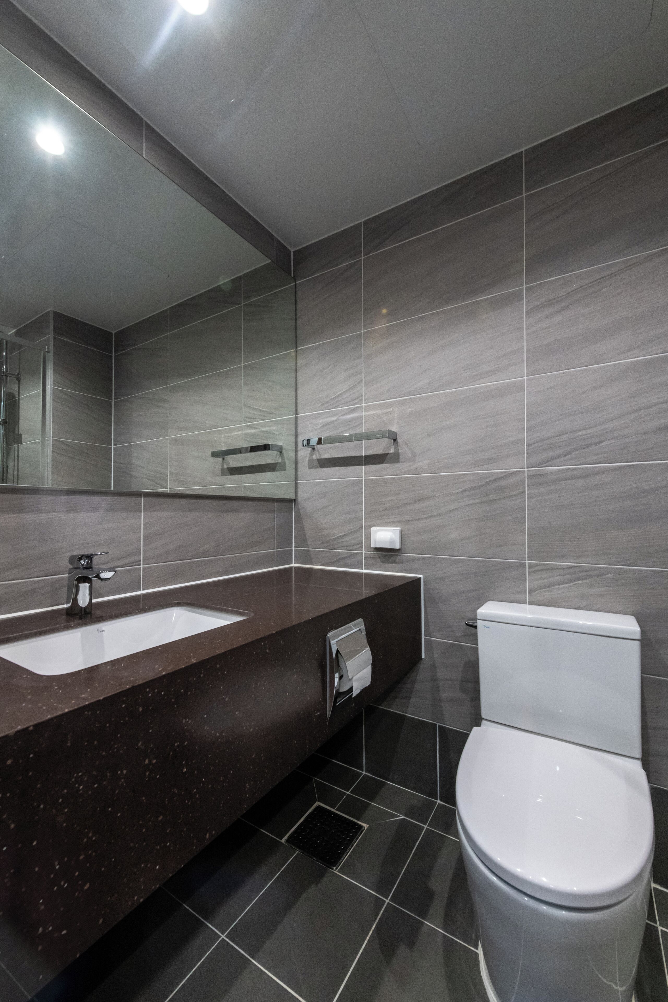 Un baño moderno con encimera de granito oscuro, lavamanos blanco, espejo y retrete.