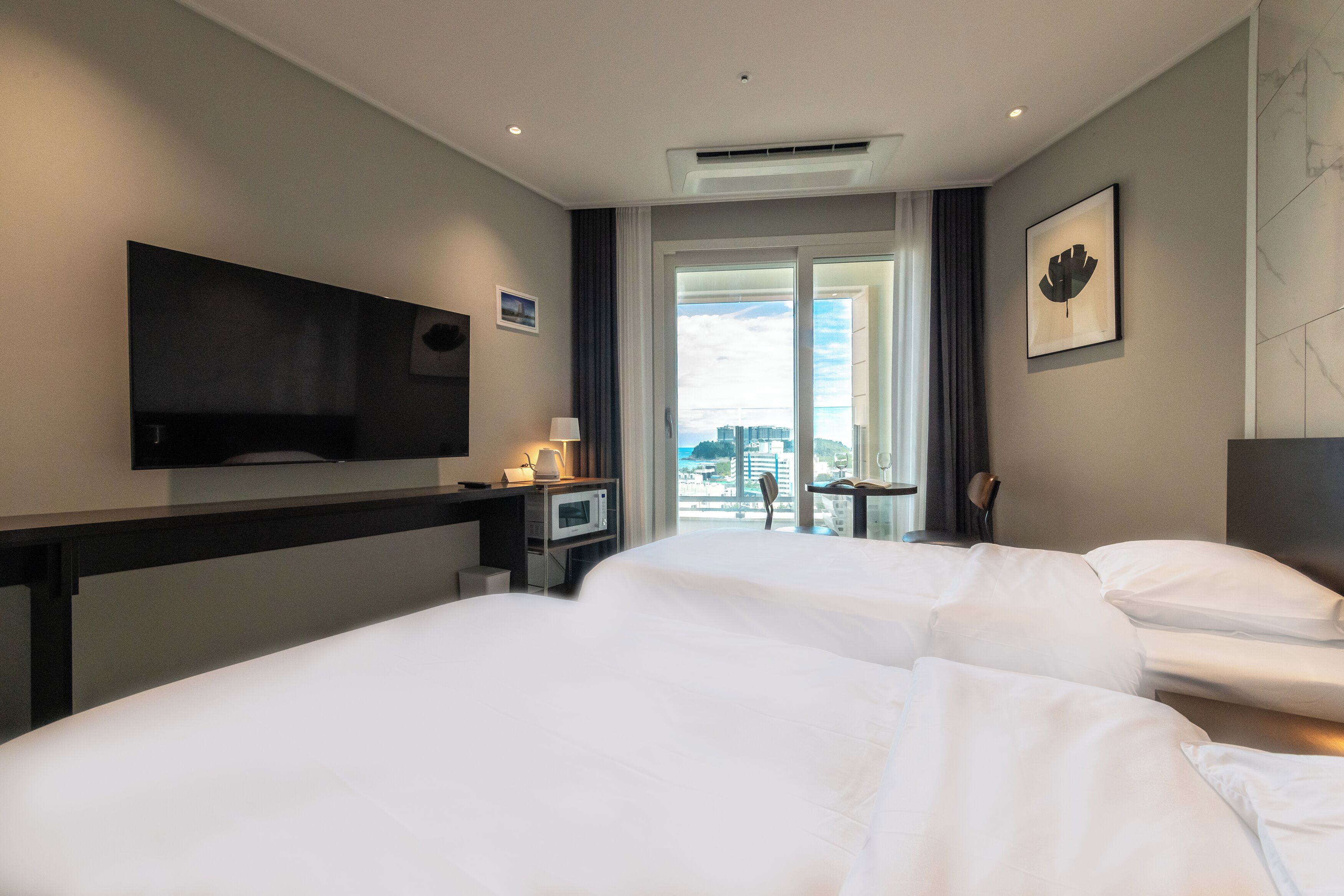 A hotel room with two beds, a TV, a desk with a lamp, and a view of the city.
