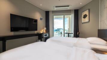 A hotel room with two beds, a TV, a desk with a lamp, and a view of the city.