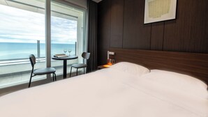Ein Hotelzimmer mit einem großen Bett, einem kleinen Tisch mit zwei Stühlen, einem Nachttisch mit Lampe und einem gerahmten Kunstwerk an der Wand.