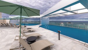 Ein Poolbereich auf dem Dach mit Liegestühlen, Sonnenschirmen und Blick aufs Meer.