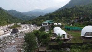 A mountainous landscape with a river, a house with a green roof, and several dome-shaped structures. - Nestonature Glamping Dharamshala (Dharamshala)