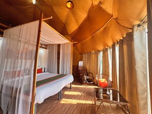 Ein Zeltraum mit Bett, Glastisch, Korbsesseln und Himmelbett.