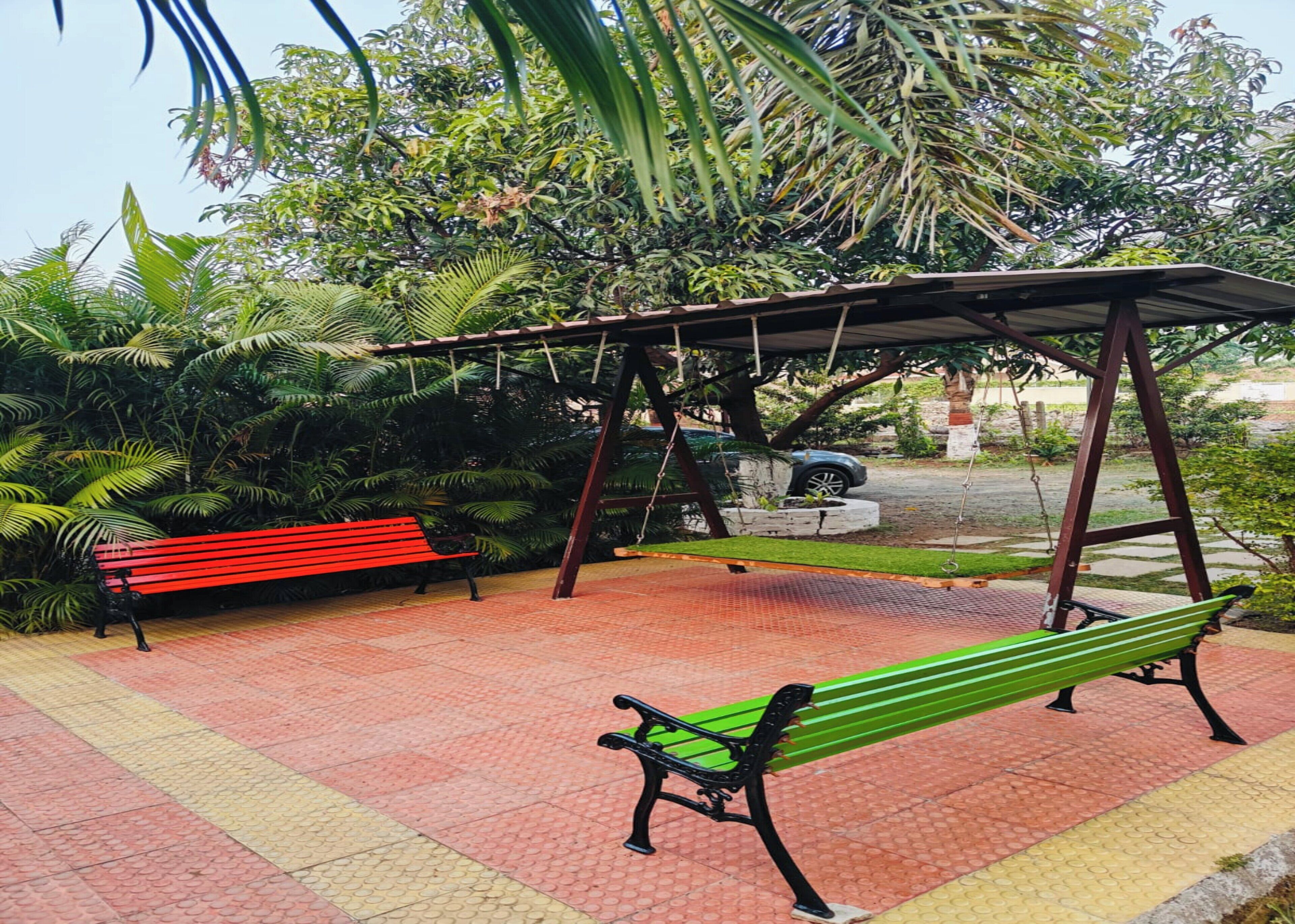 A park with two benches, one red and one green, under a wooden swing structure.