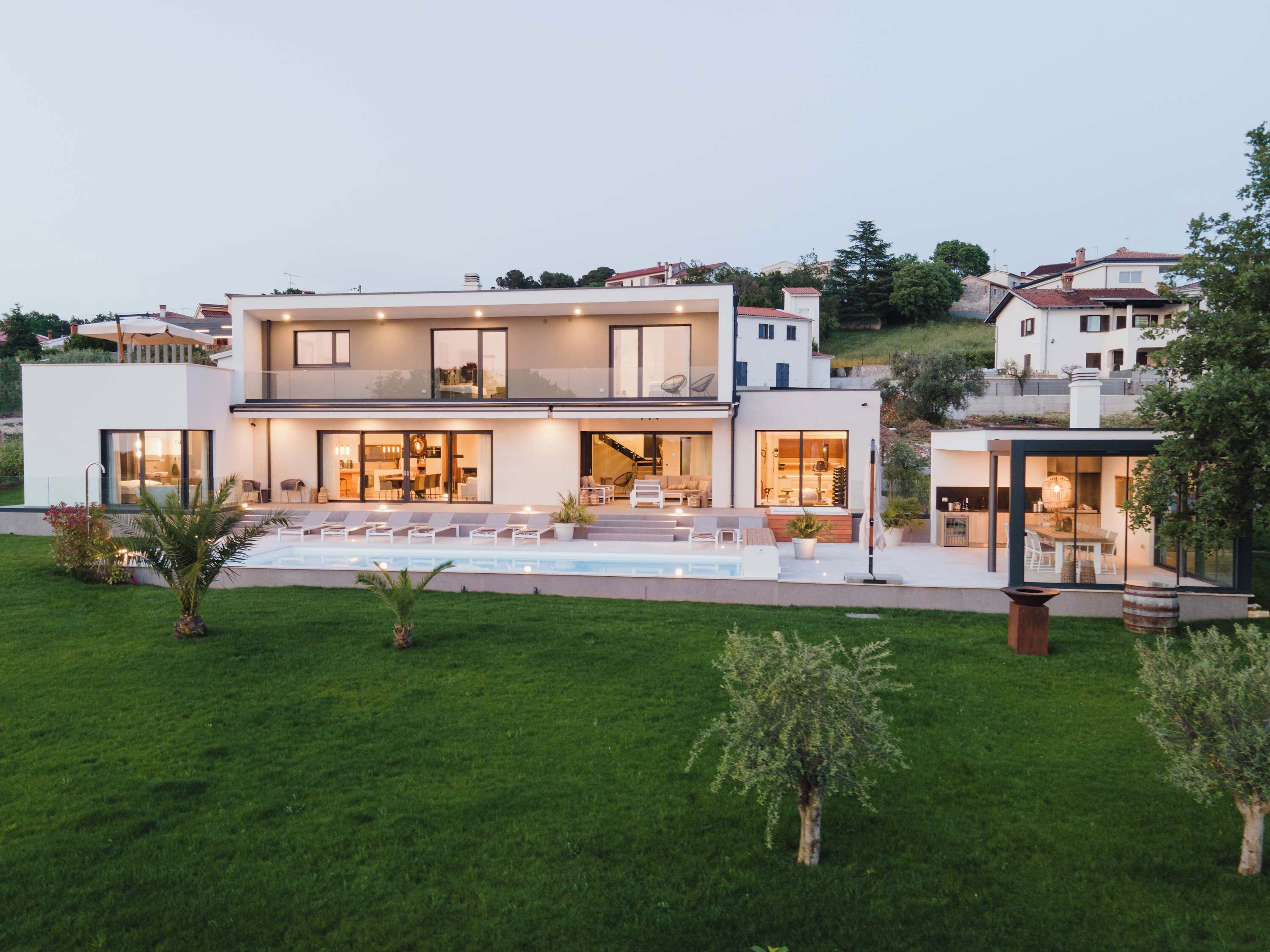 A modern two-story house with a large outdoor swimming pool, a covered patio, and a well-maintained lawn.
