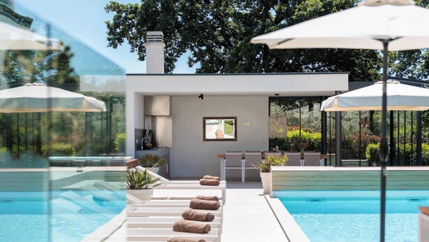 Una zona de piscina moderna amb gandules i ombrel·les, vista clara de la piscina i un petit espai d'estar amb una finestra.