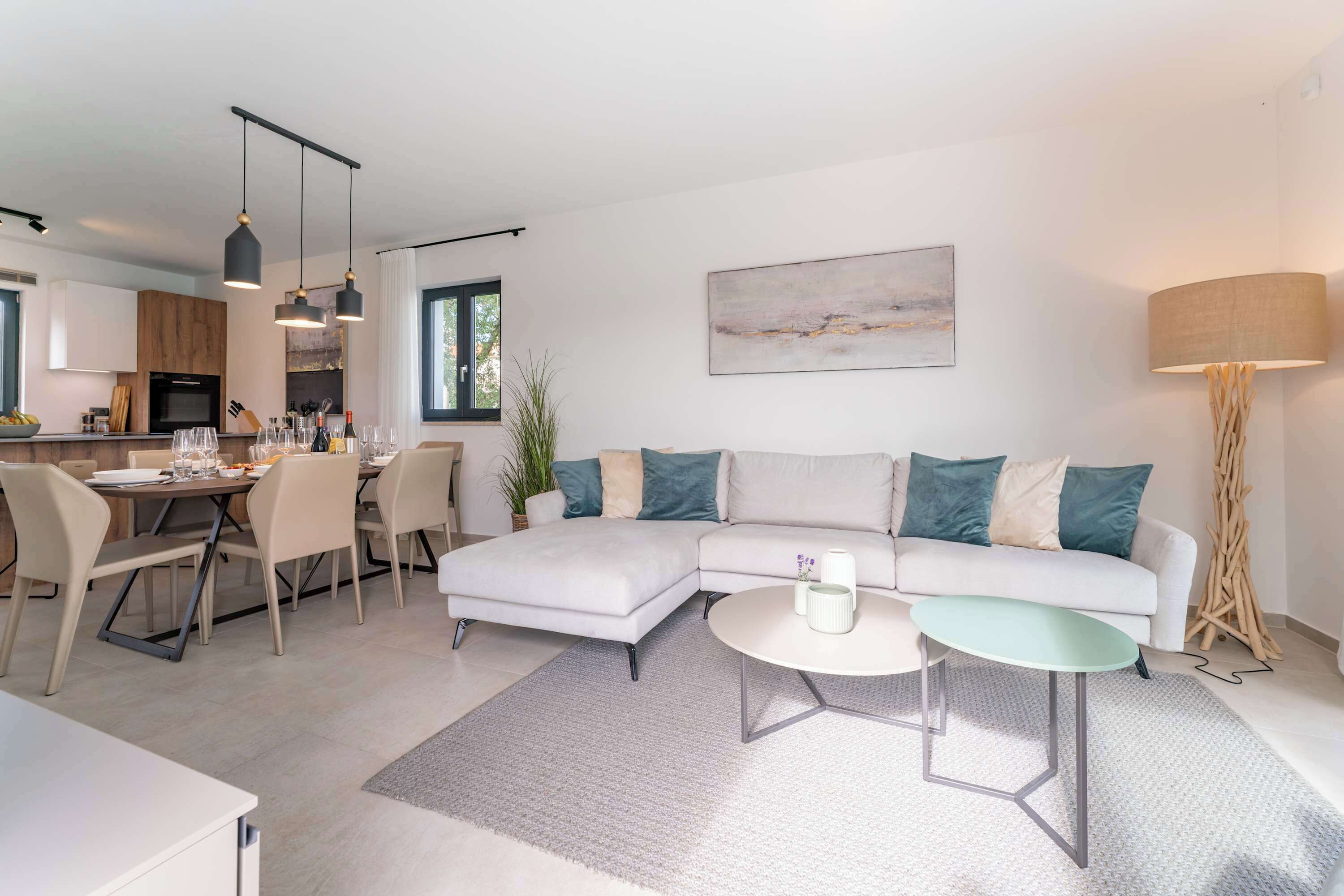 Una sala de estar moderna con un sofá seccional, un comedor con mesa y sillas, y una cocina al fondo.