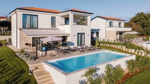 Ein modernes, zweistöckiges Haus mit Pool, Gartenmöbeln und einem gepflegten Garten.