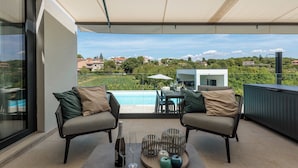 Ein Balkon mit zwei Stühlen, einem Tisch und Blick auf ein Schwimmbad und Grünflächen.