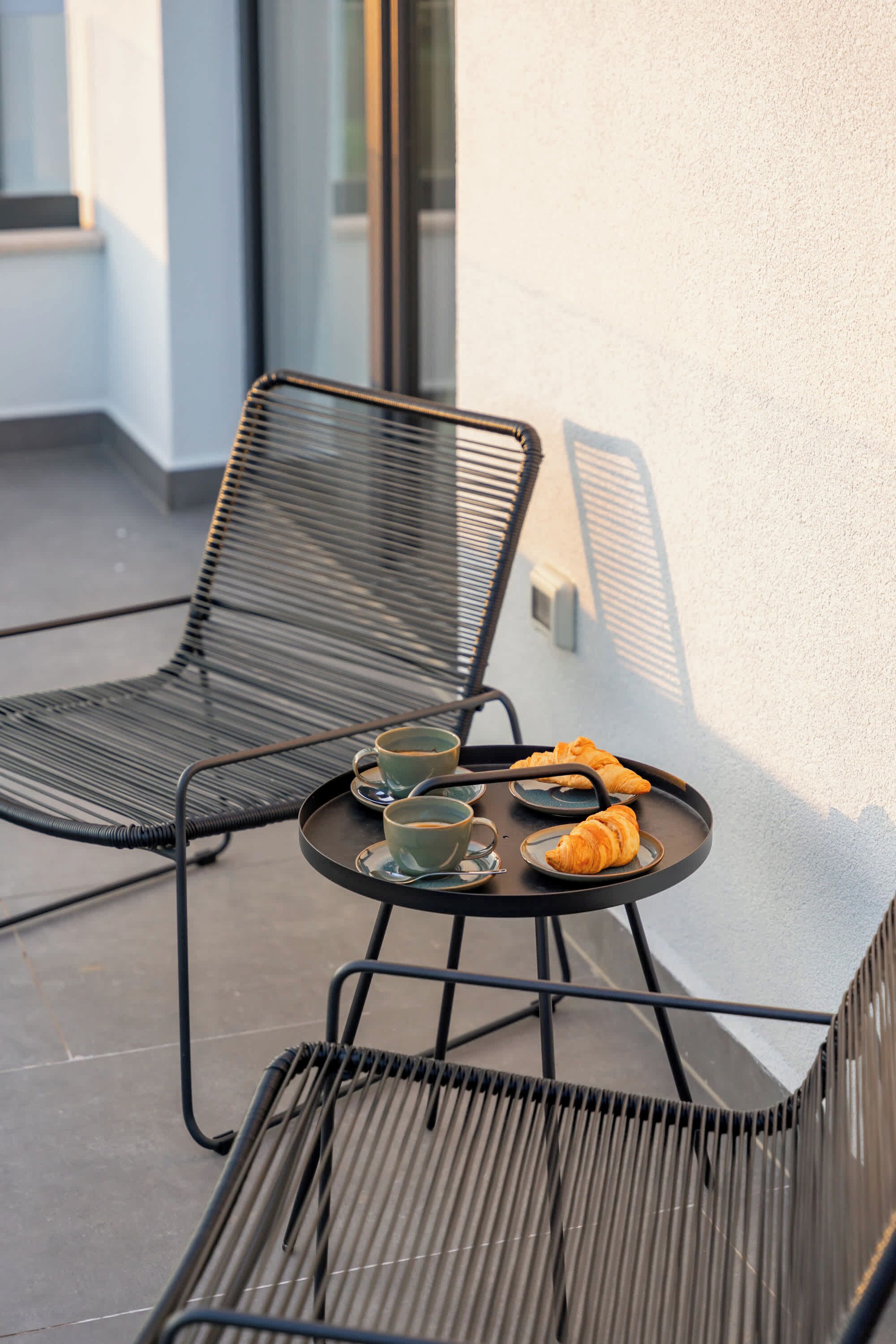 A metal-framed outdoor seating area with a table, two chairs, and a tray with croissants and cups.
