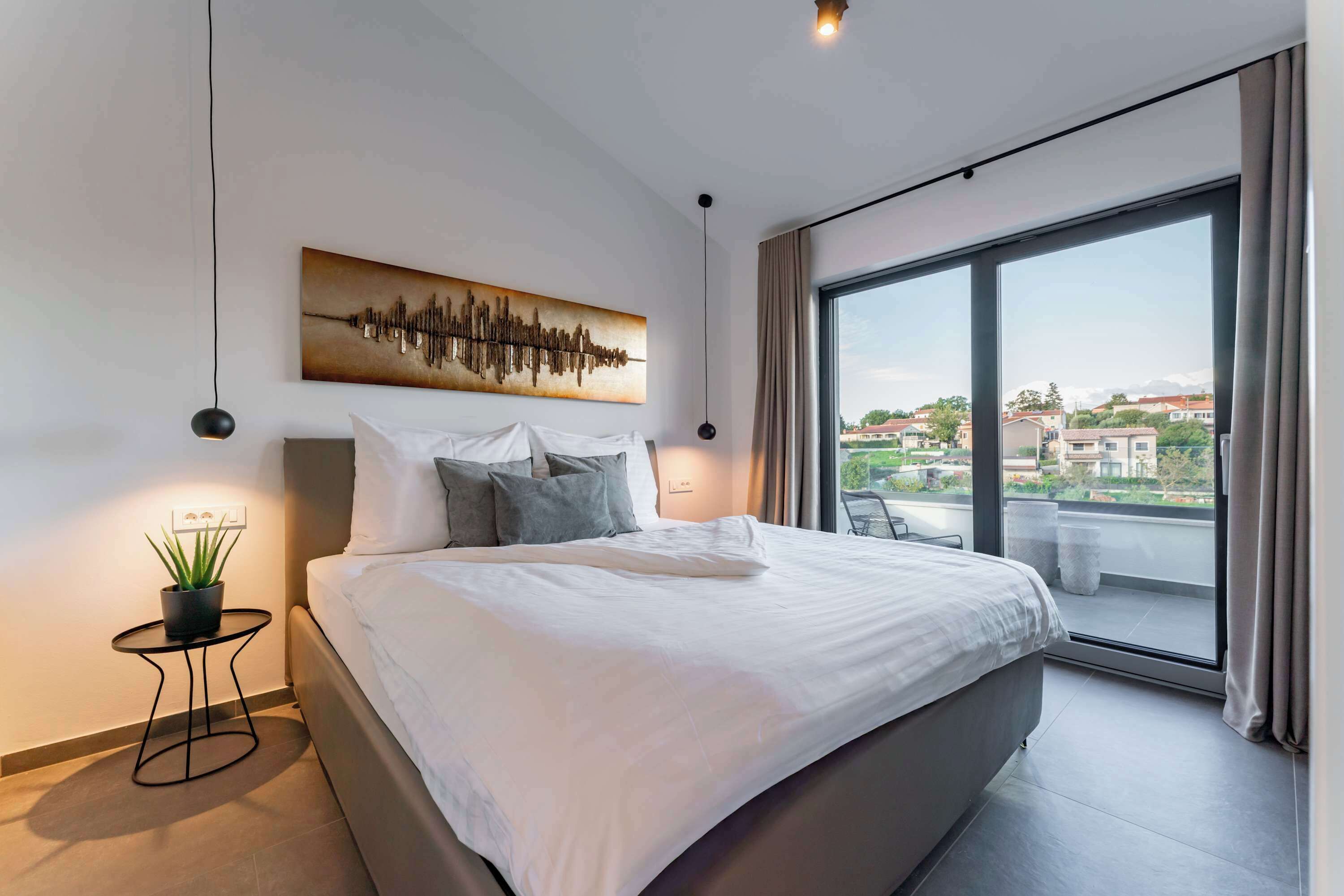 A modern bedroom with a large bed, a cityscape view through a large window, a wall-mounted sound wave art piece, and a small side table with a plant.