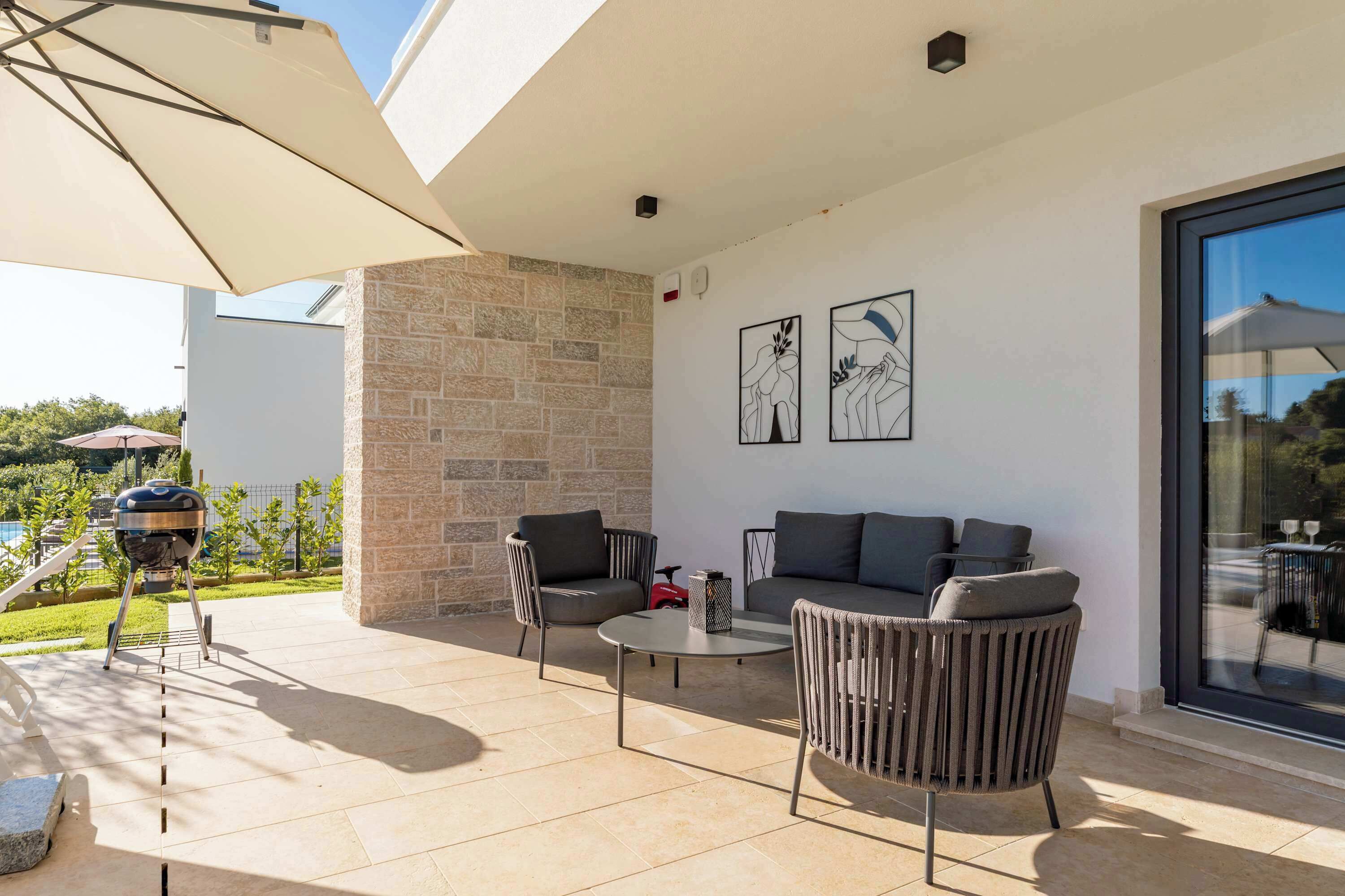 An outdoor patio with a stone wall, a barbecue grill, and seating with a glass wall and artwork.