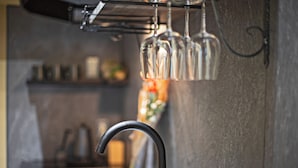 Una cocina con un grifo moderno, una tetera y una estantería para vinos con copas.
