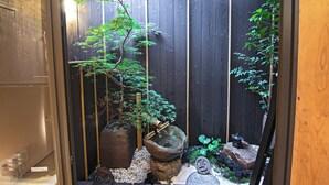 Un jardín japonés tradicional con una cerca de madera, una pila de piedra y diversas plantas.