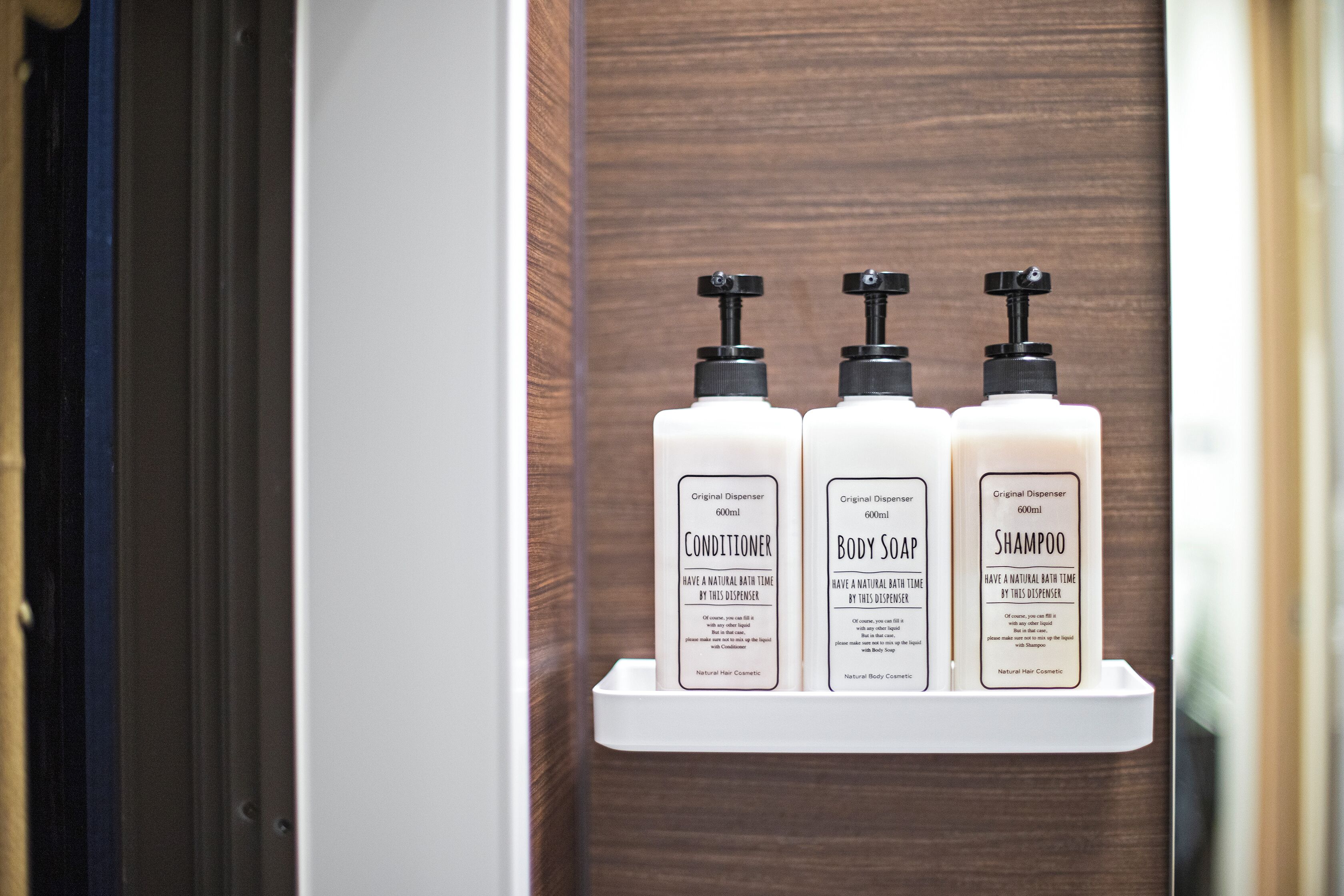 A bathroom shelf with three bottles of toiletries: conditioner, body soap, and shampoo.