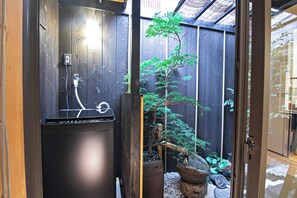 A compact room with a built-in washer and dryer, a small bonsai tree, and a wooden fence. - Tokinoyado Kamishichiken (Kyoto)