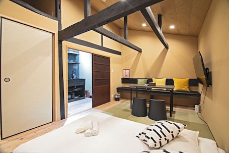 A bedroom with a bed, a sofa, a TV, and a wooden ceiling structure.