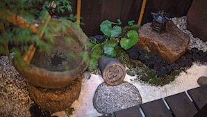 Un jardín con una planta en maceta, un farol decorativo y una piedra con un símbolo.