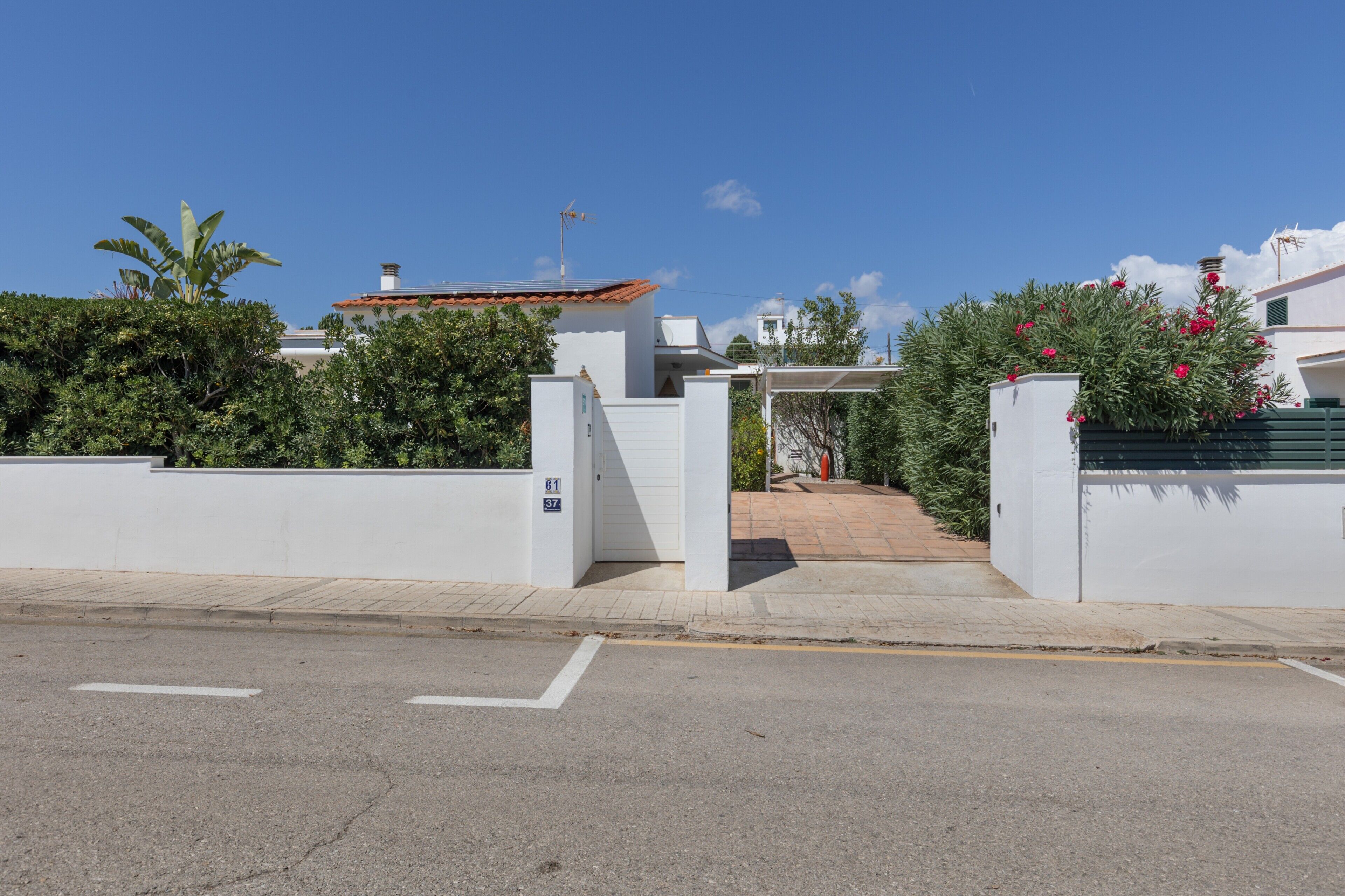A gated residential area with a clear sky, a paved road, and a white building with a red roof.