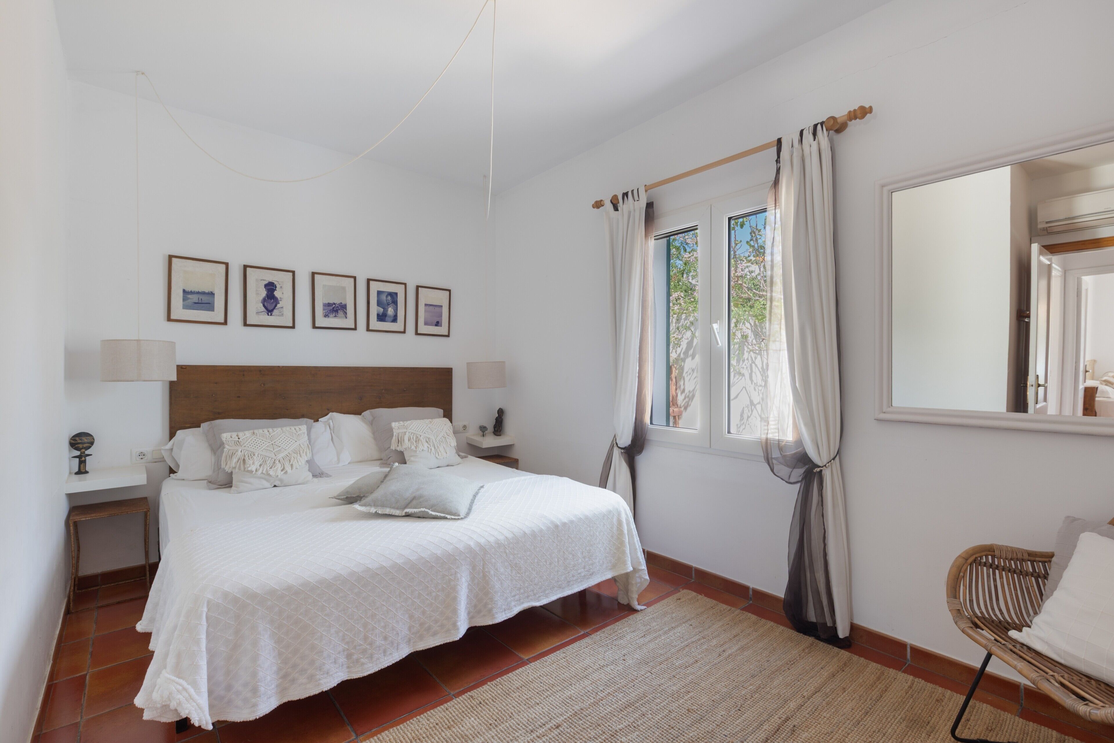A bedroom with a bed, bedside tables, a chair, a window with curtains, and framed pictures on the wall.