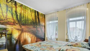 Un dormitorio con un mural de un arroyo en el bosque, una cama con ropa de cama floral y una ventana con cortinas de gasa.