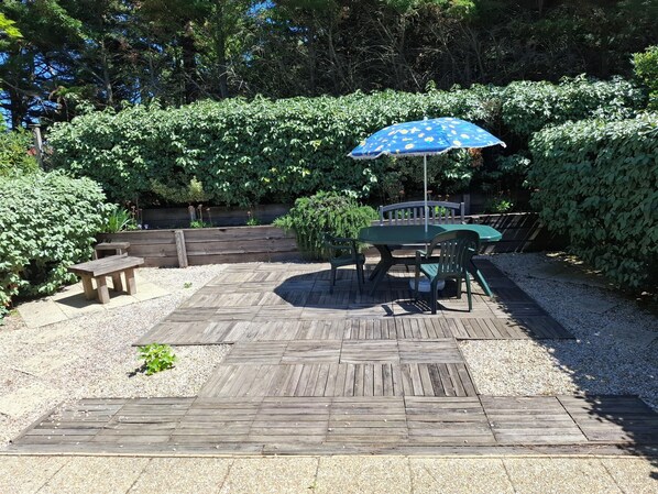 A wooden deck with a table and chairs, surrounded by a hedge and a wooden fence.