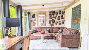 Un salon moderne avec un canapé d’angle marron, une table basse ronde et un téléviseur posé sur un bureau en bois.