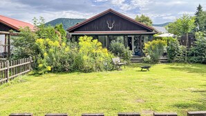 Un chalet rustique avec un toit en métal, entouré d’une végétation luxuriante et sous un ciel dégagé.