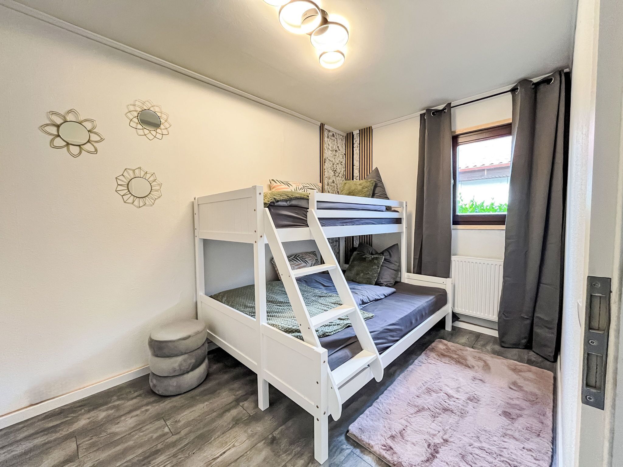 A bunk bed room with a view of greenery outside, a radiator, and decorative wall art.
