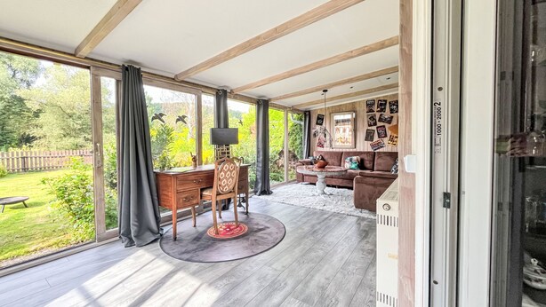 Une pièce spacieuse dotée d’une grande porte-fenêtre coulissante donnant sur un jardin, d’un bureau en bois avec une chaise, d’une table basse ronde et d’un canapé marron.